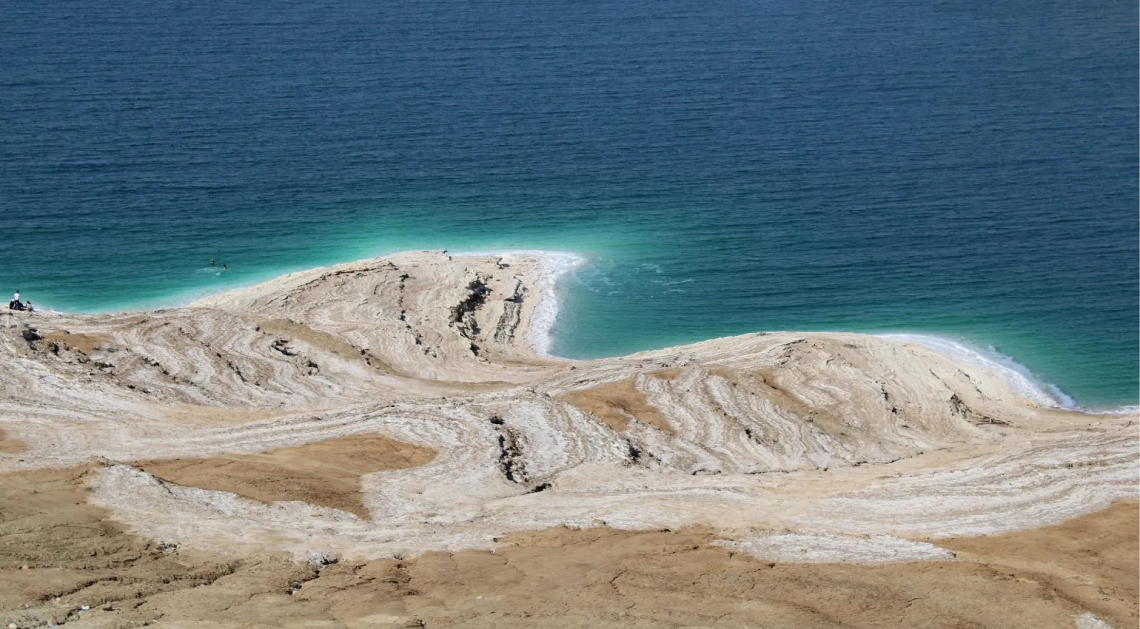 Aerial view of the Dead Sea shoreline showing pale mineral flats meeting turquoise water