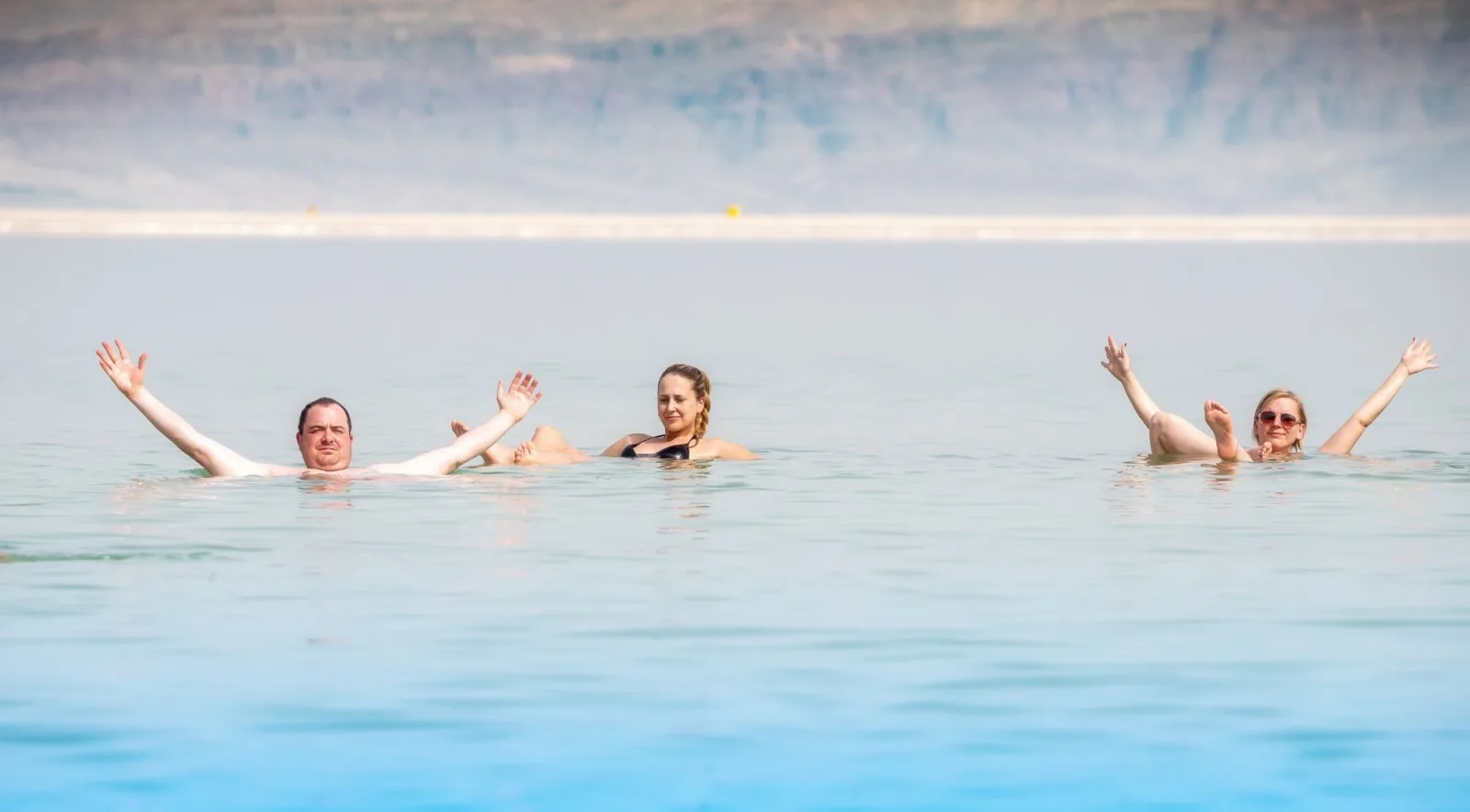 Three people floating on their backs in the Dead Sea with their arms raised out of the water