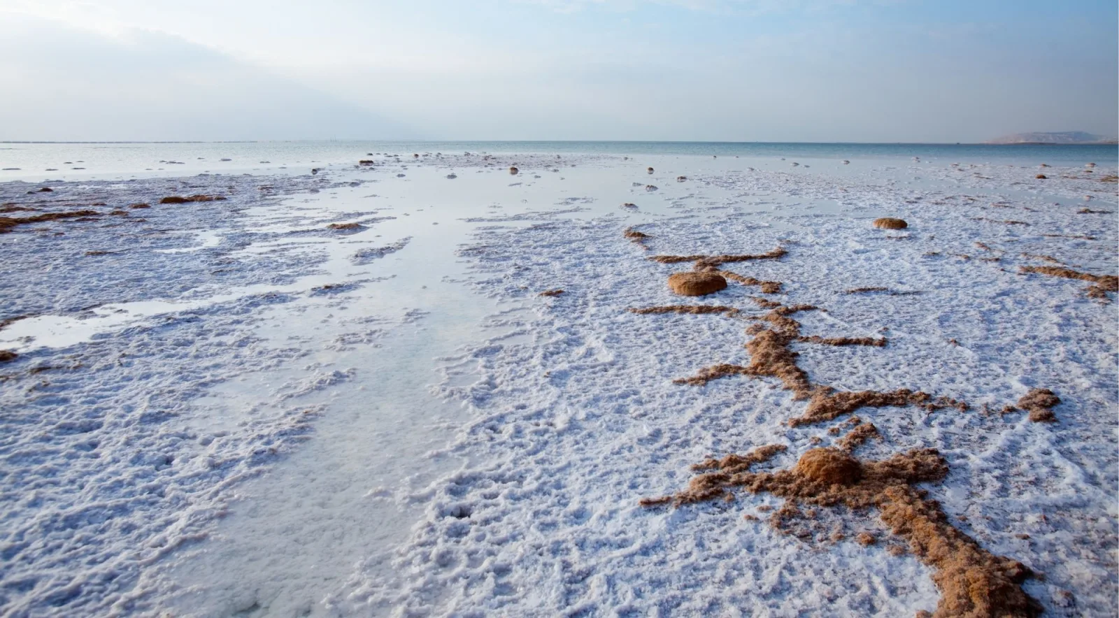 Wide expanse of white salt flats along the Dead Sea shore under a hazy sky
