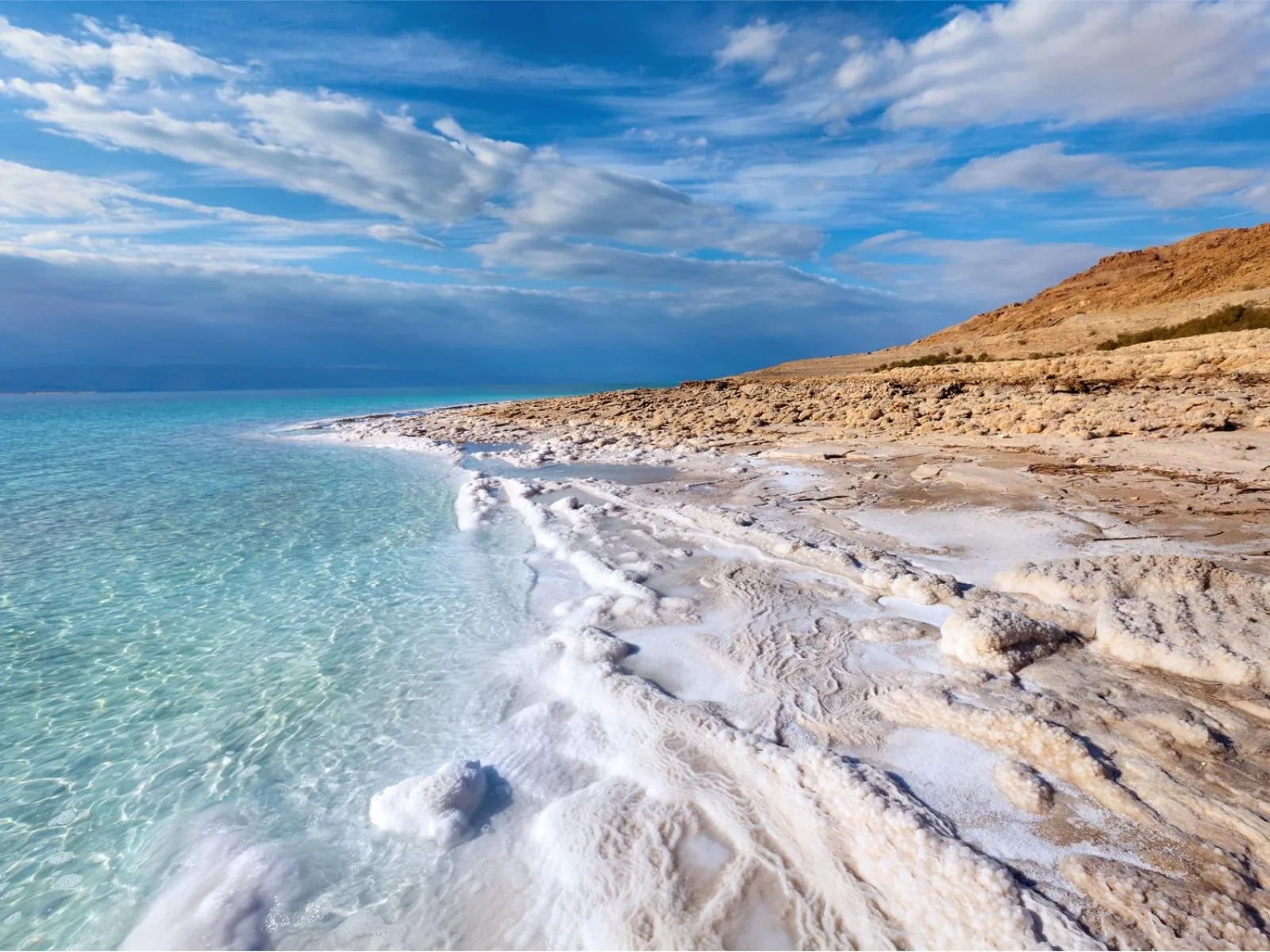 Crystallised salt shelf running along the Dead Sea shore beside clear turquoise water