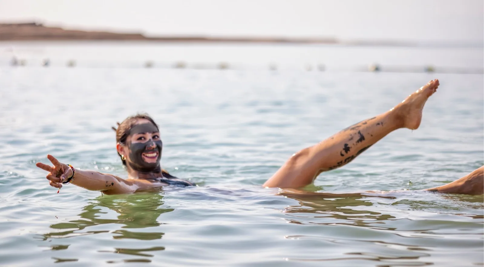 A woman floating in the Dead Sea with black mineral mud on her face and legs