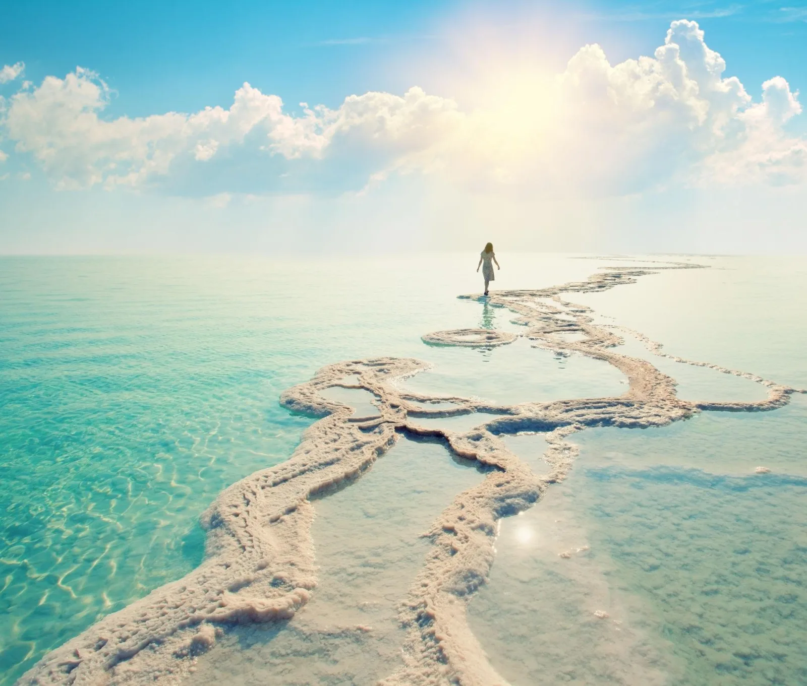 Salt ridges snaking out into shallow turquoise Dead Sea water under a bright sky
