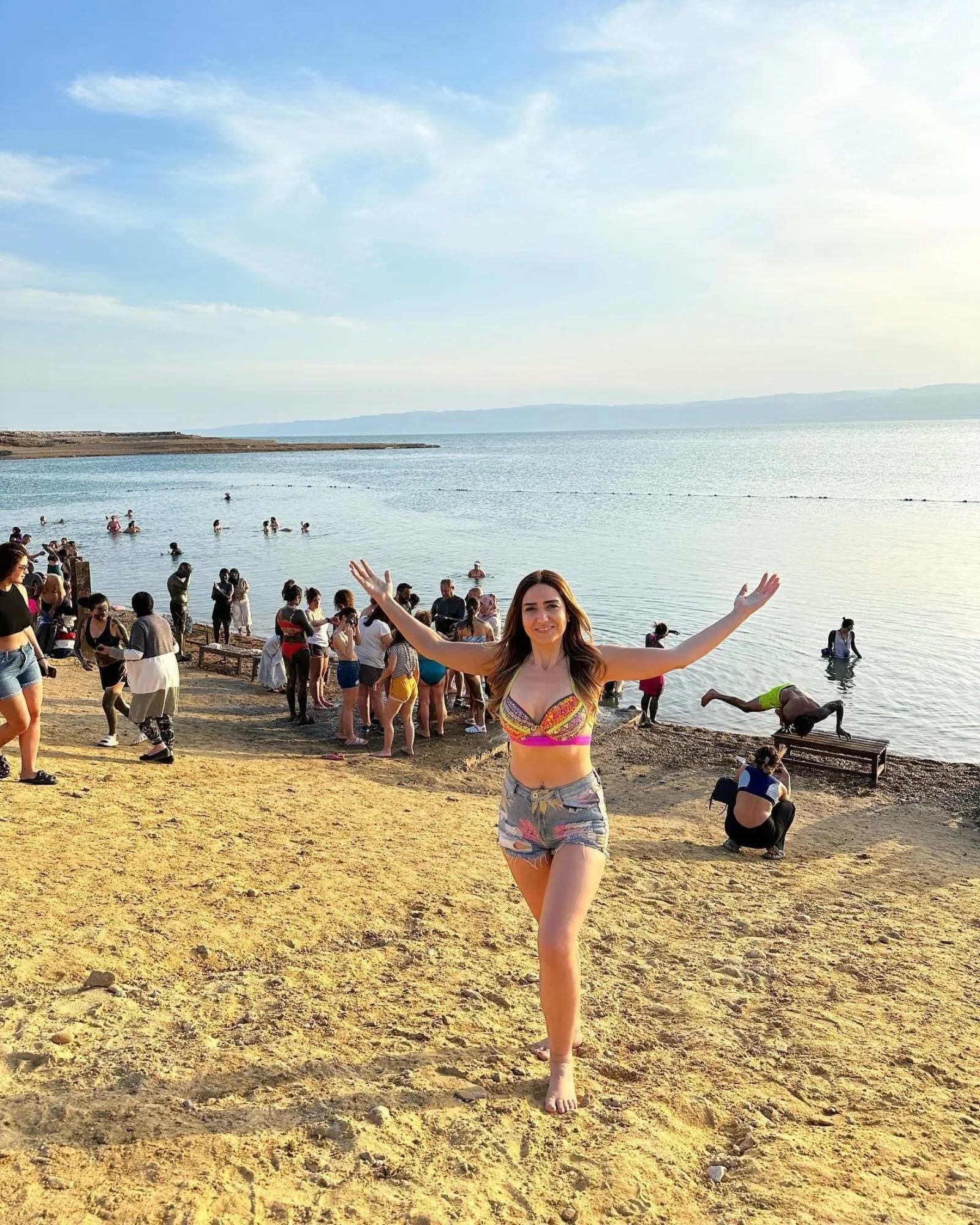 Visitors coating themselves in black mud on the Dead Sea shore in late afternoon light
