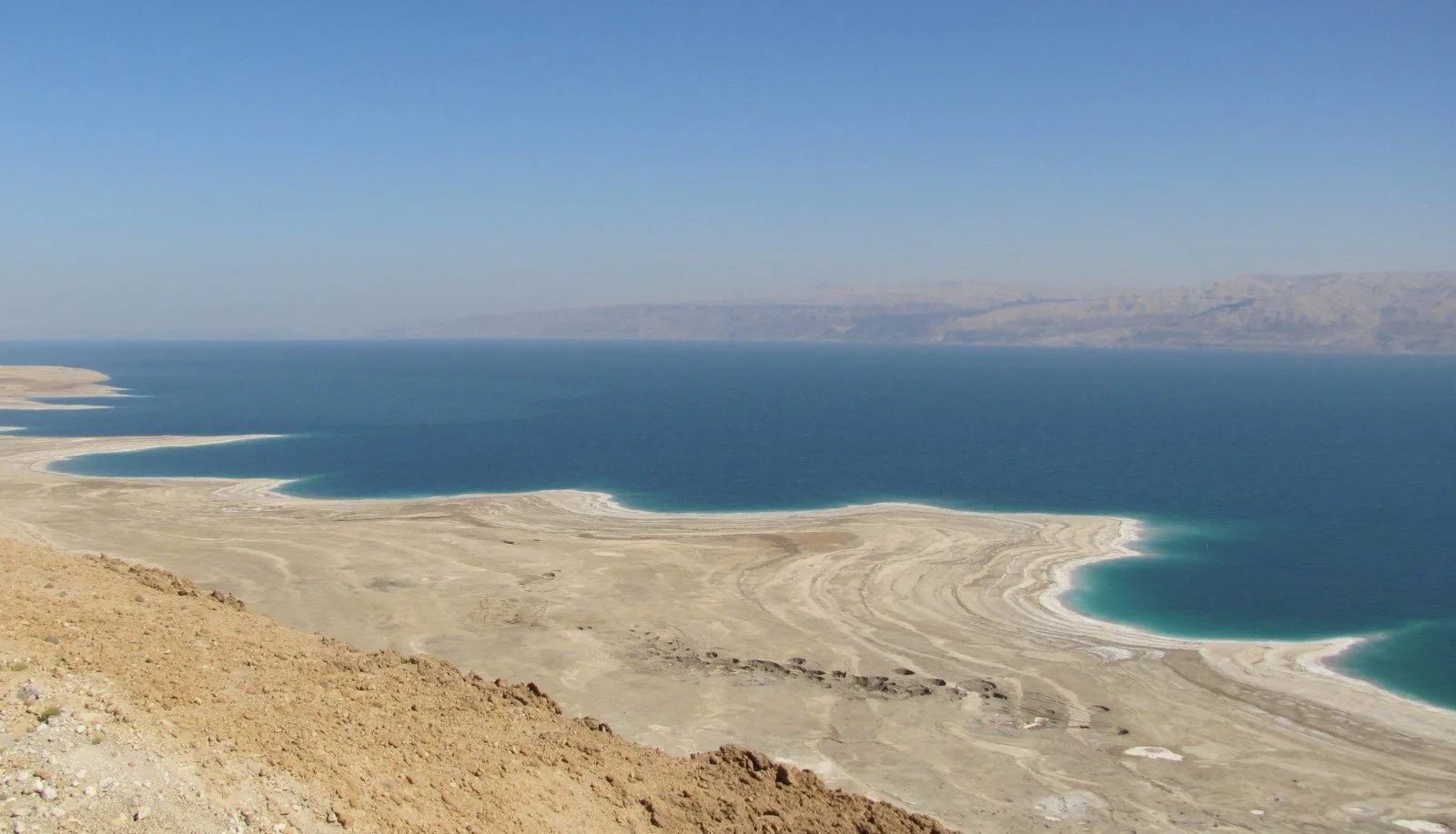 The Dead Sea seen from the escarpment road, pale mineral flats meeting deep blue water