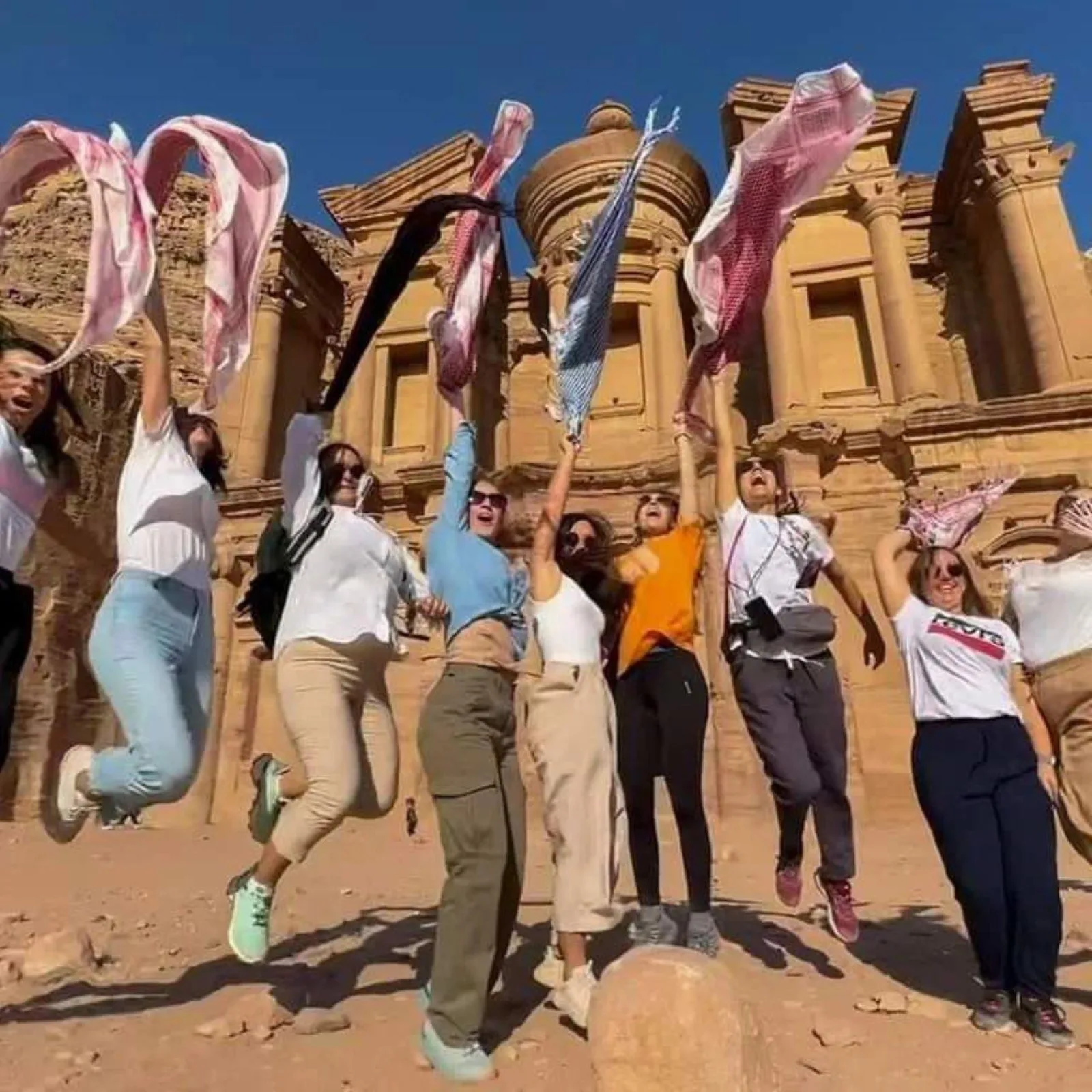 A tour group jumping in front of the Monastery at Petra with keffiyehs raised
