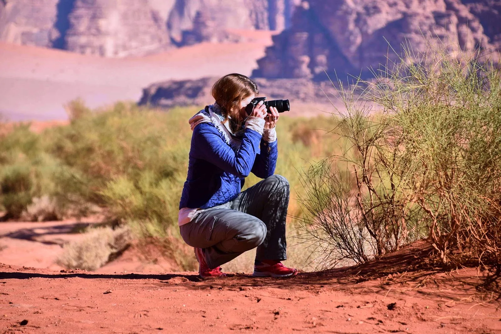 A traveller photographing the desert scrub and red sand of Wadi Rum