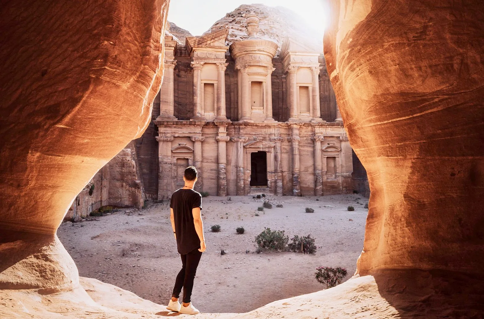 A visitor looking out at Petra's Monastery from the shaded rock opening opposite it