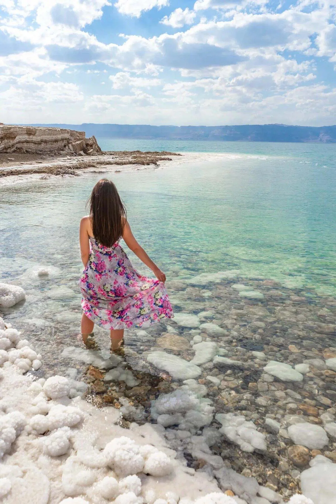 A woman standing in the shallows on the Jordanian Dead Sea shore, salt crust underfoot