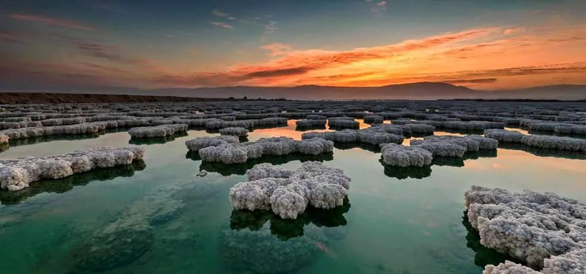 Salt flats at the Dead Sea reflecting an orange sunset over the hills