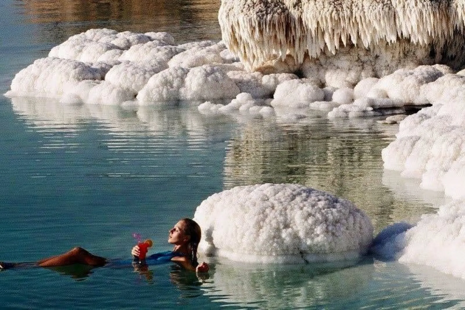 A woman floating in the Dead Sea beside cauliflower-shaped salt boulders